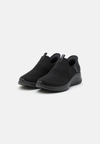 Sorte slip-on sko med en strikket overdel, teksturert midtfotdel og en gummisåle med et subtilt mønster.