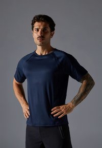 Tumši zila sporta t-krekls no gludas, mitrumu aizvairojošas auduma ar apaļu apkakli un raglāna piedurknēm. Šaura piegriezuma dizains ar smalku spīdumu.