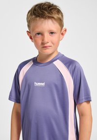 Lila sportst-shirt med rosa sidodetaljer, korta ärmar och "hummel PERFORMANCE"-logotyp på bröstet. Mjuk tygstruktur.