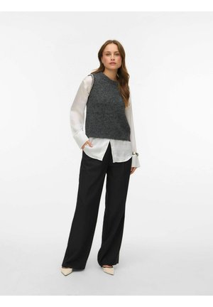 Haut sans manches en laine grise tricotée porté sur une chemise blanche à boutons, associé à un pantalon noir à jambes larges et des chaussures crème à bout pointu.