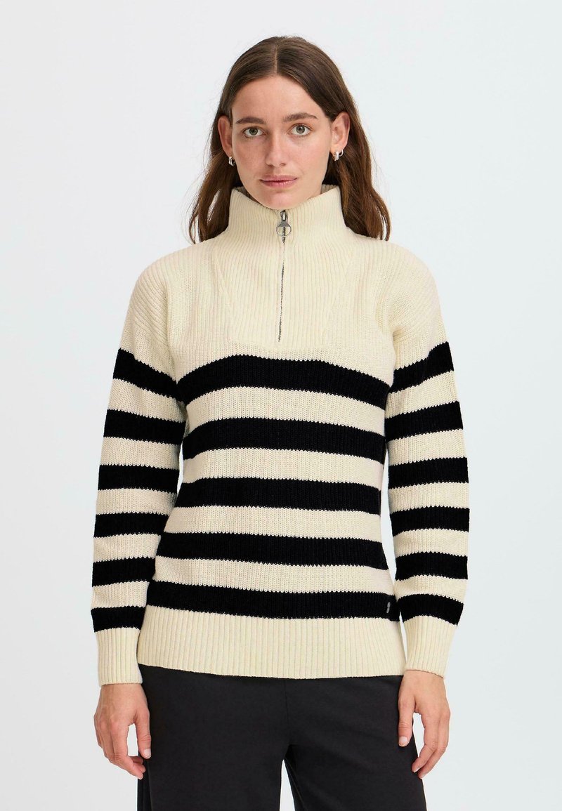 Maglione a maglia a righe crema e nere. Collo alto con chiusura a zip, polsini e orlo a costine. Tessuto morbido, vestibilità ampia.