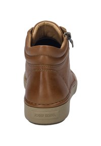 Bottine en cuir marron avec fermeture éclair et semelle en caoutchouc beige. Présente une texture lisse et des coutures visibles. Étiquette de la marque sur le talon.