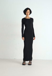 Abito lungo a maniche nere con costine, dalla silhouette aderente fino alla caviglia, abbinato a sandali platform neri chunky.