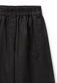 Zwarte broek met elastische tailleband en een gladde textuur, voorzien van zijzakken en ton-sur-ton stiksels. Eenvoudig ontwerp zonder versieringen.