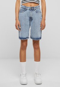 Shorts en denim bleu clair avec une coupe droite, délavés, et légèrement effilochés à l'ourlet. Associés à des baskets blanches et des chaussettes blanches côtelées.