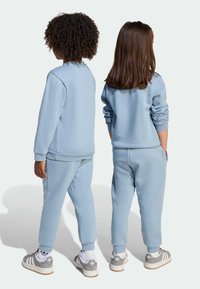 Svetlo modra majica in hlače iz mehkega blaga, s rebrastimi manšetami in pasom, obuti z sivimi supergami.