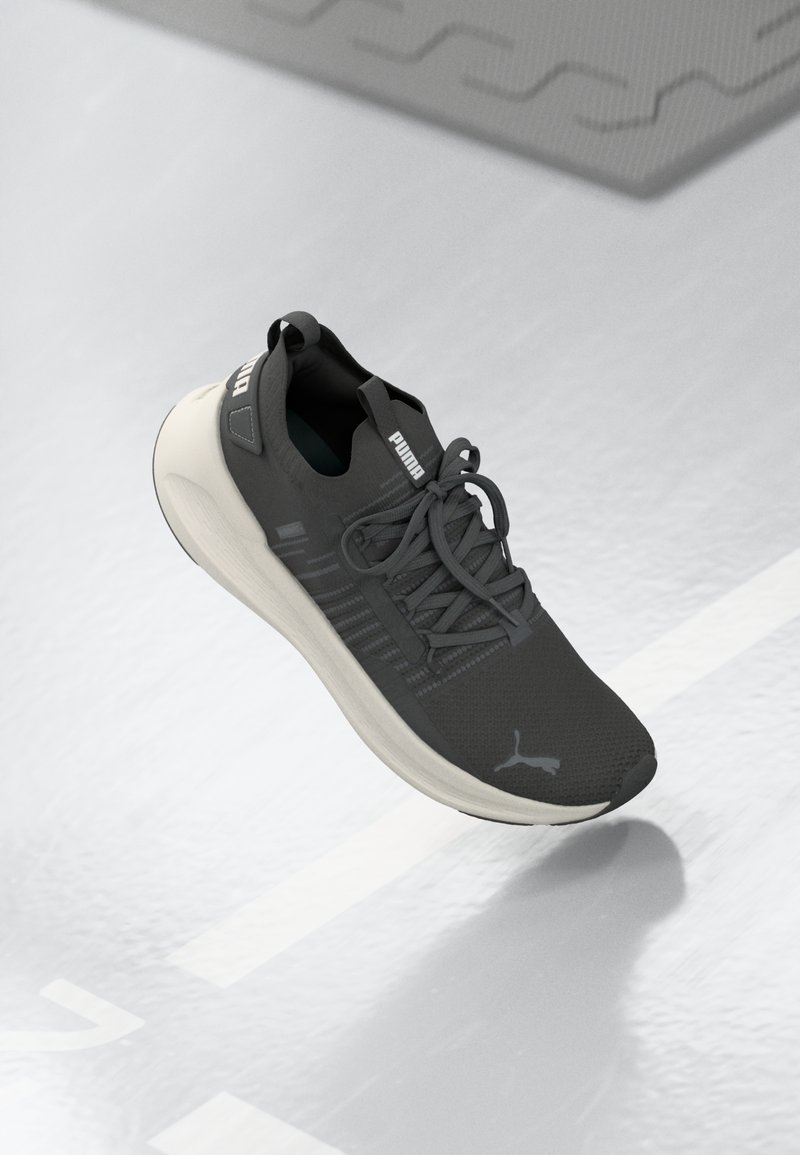Chaussure de sport en maille gris foncé, avec une semelle et des lacets gris clair. Marquage Puma notable sur le côté et la languette. Surface texturée.