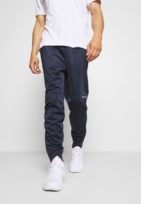 Navy träningsbyxor med elastiska muddar, en avslappnad passform och sidostripes. Kombinerat med en vit t-shirt och vita sneakers.