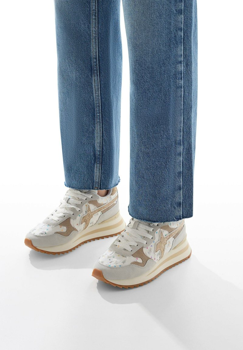 Sneakers bianchi, beige e grigio chiaro con motivi testurizzati, dotati di suola in gomma e lacci, abbinati a pantaloni in denim blu cropped.