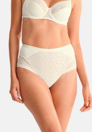 Femme portant une culotte taille haute en résille blanche et un soutien-gorge blanc à armatures assorti, montrant le ventre et le haut des cuisses.