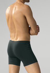 Ciemnozielone bawełniane szorty typu boxer o miękkiej fakturze, z elastycznym paskiem w talii i dopasowanym fasonie, widok z boku.