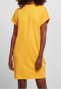 Żółta bawełniana sukienka w stylu t-shirt z luźnym krojem, krótkimi, podwiniętymi rękawami i okrągłym dekoltem. Posiada małą metkę na dolnej stronie.