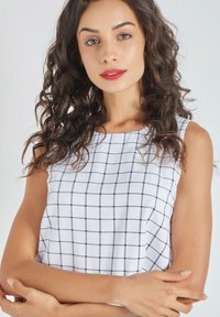 Top sin mangas blanco con un patrón de cuadrícula en azul marino. Tela suave con cuello redondo, que presenta un diseño limpio y minimalista.