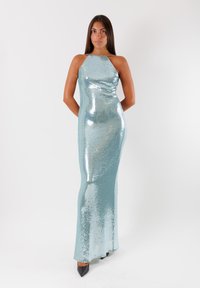Abito da sera in paillettes di colore azzurro chiaro con silhouette aderente. Presenta un collo all'americana e scende fino a terra. Tacchi neri a punta completano il look.