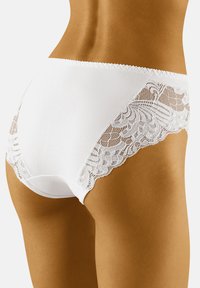 Witte slip met een gladde stof en ingewikkelde kantdetails aan de zijkanten. Het ontwerp heeft zachte randen en een klassieke snit.