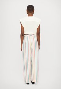 Bela pletena kratka majica z širokimi rokavi, v kombinaciji z ohlapnimi, večbarvnimi črtastimi hlačami visoko pasu. Gladka tekstura, pastelni toni.