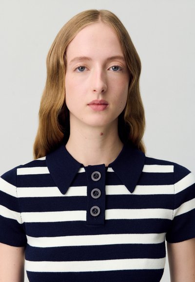 Polo a righe navy e bianche con colletto, dotato di quattro bottoni neri e design aderente. Il tessuto ha una texture liscia.