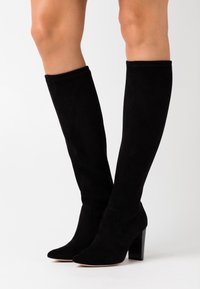 Botas altas de ante negras hasta la rodilla con punta afilada y tacón ancho, que presentan una textura suave y un diseño sin costuras.