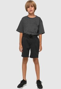 Shorts noirs en coton avec une taille élastique, associés à un t-shirt gris à manches courtes et des chaussures de sport noires. Texture lisse et design simple.