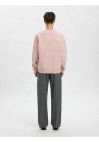 Lys rosa genser med lange ermer, rund hals og ribbet kant, kombinert med grå vide bukser og svarte sko.