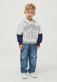 Szary hoodie z krótkim rękawem z nadrukiem "BOSTON 88" i granatowymi akcentami. W połączeniu z jasnoniebieskimi dżinsami z przetarciami i białymi trampkami.