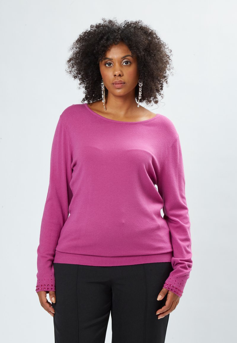 Rosa gerippter Pullover mit einem lässigen Bootsausschnitt, langen Ärmeln mit strukturierten Bündchen, kombiniert mit schwarzen maßgeschneiderten Hosen.