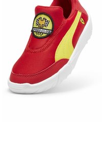 Punaiset liukupohjaiset kengät, joissa on keltainen sivuviiva ja ympyräinen musta ja keltainen tägi, jossa lukee "SPEED CLUB". Valkoinen teksturoidusta kumista valmistettu pohja.