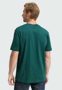 Camiseta de algodón verde con mangas cortas, cuello redondo y corte relajado. Sin patrones; diseño simple sin logotipos ni acentos visibles.