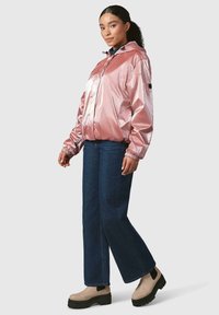 Rózsaszín, fényes, könnyű dzseki kapucnival, elasztikus mandzsettával és húzózsinórral. Sötétkék, laza szabású farmernadrággal és bézs, vastag bokacsizmával párosítva.