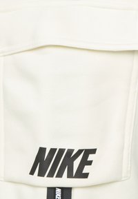 White Nike fabric with visible stitching and a large black logo. Features include a smooth texture and a rectangular pocket design.