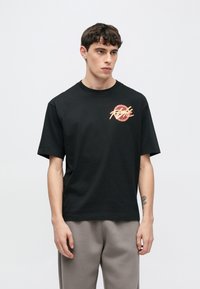 Fekete pamut póló kerek nyakkivágással és rövid ujjakkal. Színes grafikus logó található a bal mellrészen. Sima textúrájú.