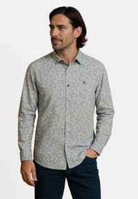 Lichtblauwe shirt met lange mouwen, met een bloemenpatroon, knopen en een klein logo op de borst; de stof heeft een gestructureerde uitstraling.