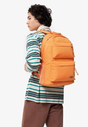Mochila naranja con dos bolsillos frontales, un acabado texturizado y correas ajustables, llevada sobre una camiseta de manga larga a rayas.