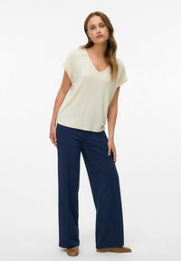 Haut beige à col en V avec des manches courtes, associé à un pantalon large marine et des chaussures plates beige. Tissu lisse avec une coupe décontractée.