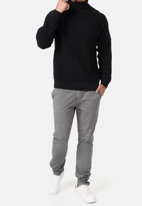 Pull noir à col roulé en maille avec texture côtelée, associé à un pantalon slim gris clair et des baskets blanches.