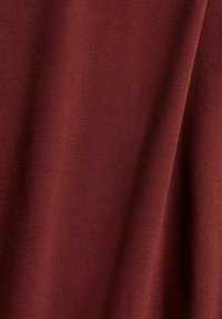 Syvä burgundinpunainen kangas, jolla on sileä ja tasainen pinta, esittää ryppyjä, jotka viittaavat pehmeyteen. Materiaali näyttää joustavalta ja tiukasti kutomalta.