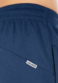Marineblå ribbede shorts med en struktureret overflade, der har en sidelomme og et hvidt "SMILODOX" logo mærke syet på fronten.