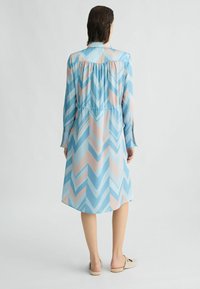 Abito azzurro chiaro con un motivo a zigzag in tonalità di rosa e blu. Presenta un colletto, maniche lunghe e una vita elasticizzata per una forma aderente.