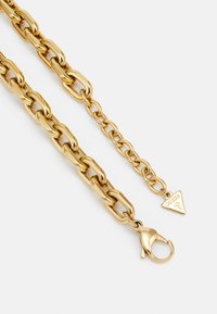 Gouden kettingaccessoire met ovale schakels, een karabijnhaak en een driehoekig label met het 'GUESS' logo. Hoge glans afwerking.