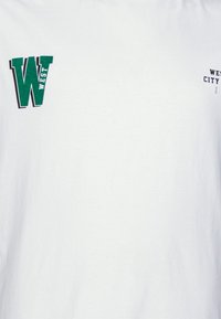 Camiseta de algodón blanca con un gran logo verde y negro con una "W" y el texto "WEST" en el lado izquierdo del pecho, y el texto "CITY" en negro en el lado derecho.
