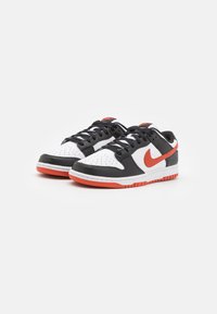 Baskets Nike avec un dessus en cuir noir et synthétique blanc, accents orange, orteil perforé et semelle en caoutchouc avec un motif de bande de roulement distinct.