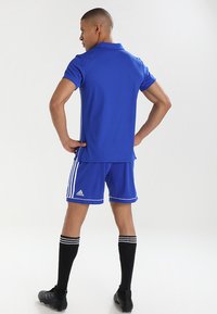 Blaues sportliches Polohemd und Shorts mit weißen Akzenten, kombiniert mit schwarzen Kniestrümpfen. Hergestellt aus glattem, leichtem Stoff.