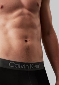 Svart undertøy med en grå Calvin Klein-logo på midjebåndet. Glatt stoff, tettsittende fasong og minimalistisk design med en subtil glans.