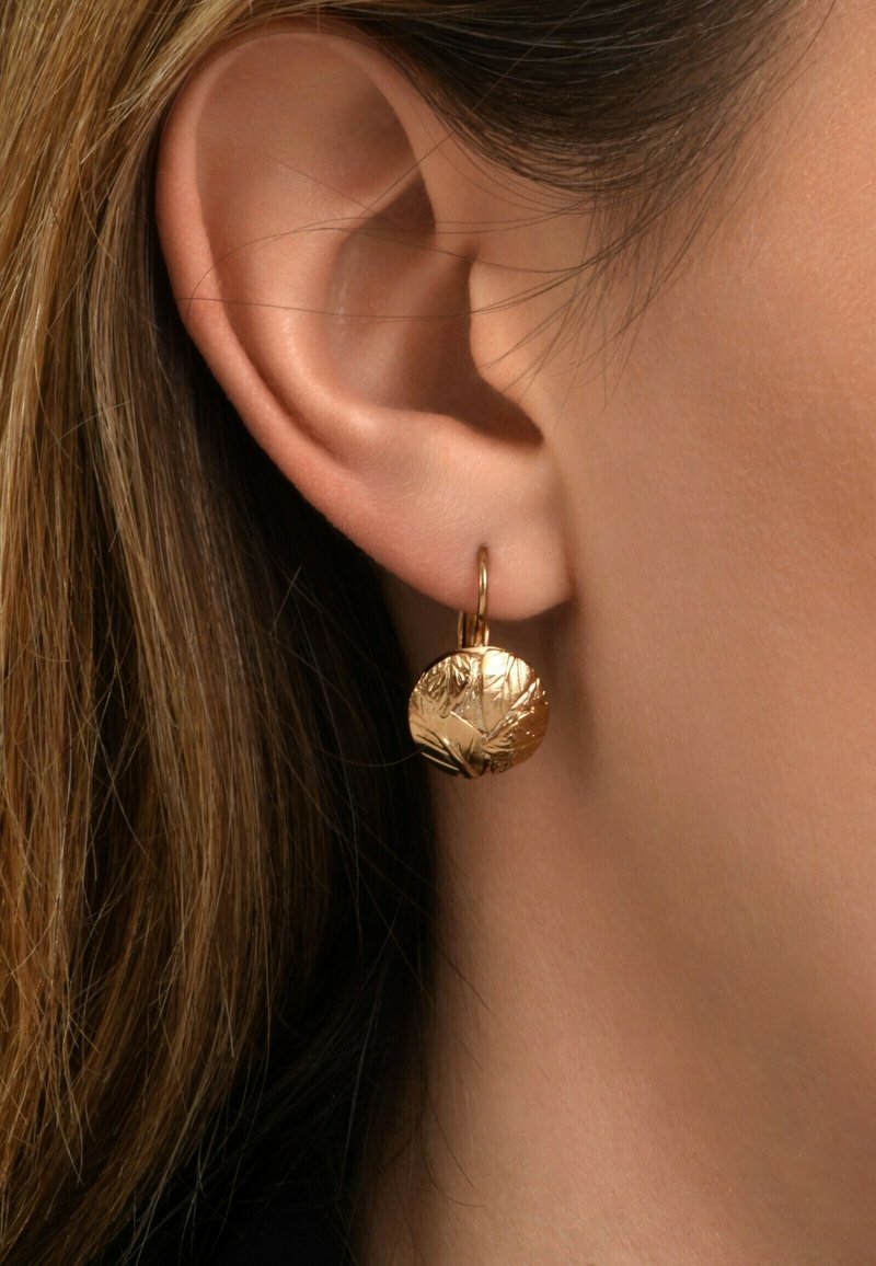 Boucles d'oreilles pendantes dorées avec un design circulaire texturé ressemblant à des feuilles. Les boucles pendulent d'un petit anneau, mettant en valeur un détail complexe.