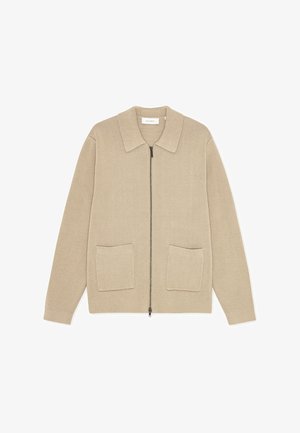 Beżowy sweter rozpinany na zamek z płaskim kołnierzem i dwoma naszywanymi kieszeniami. Charakteryzuje się fakturowanym materiałem i luźnym krojem.