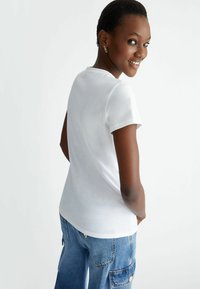 Camiseta de algodón blanca con mangas cortas y escote redondo, combinada con pantalones cargo de denim azul claro que cuentan con bolsillos laterales.