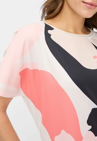 Kortærmet bluse i letvægtigt stof med et abstrakt design i koral, pink, sort og beige farver. Pæn rund halsudskæring.