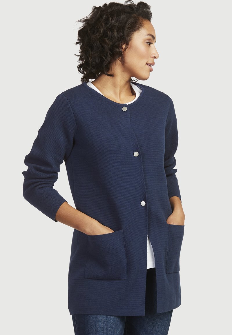 Marineblauer Cardigan aus strukturiertem Stoff, mit Rundhalsausschnitt, silbernen Druckknöpfen und zwei Fronttaschen. Mit langen Ärmeln.