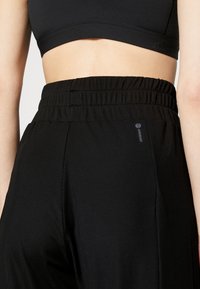 Schwarze Sporthose mit gerippter Struktur, elastischem Bund und kleinem Logo-Akzent an der Seite. Entworfen für Komfort und Flexibilität.