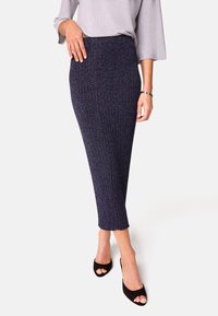 Gebreide kokerrok in donkerblauw met een geribbelde textuur, voorzien van een aansluitende taille en subtiele glans. Gecombineerd met zwarte open-tipe hakken.